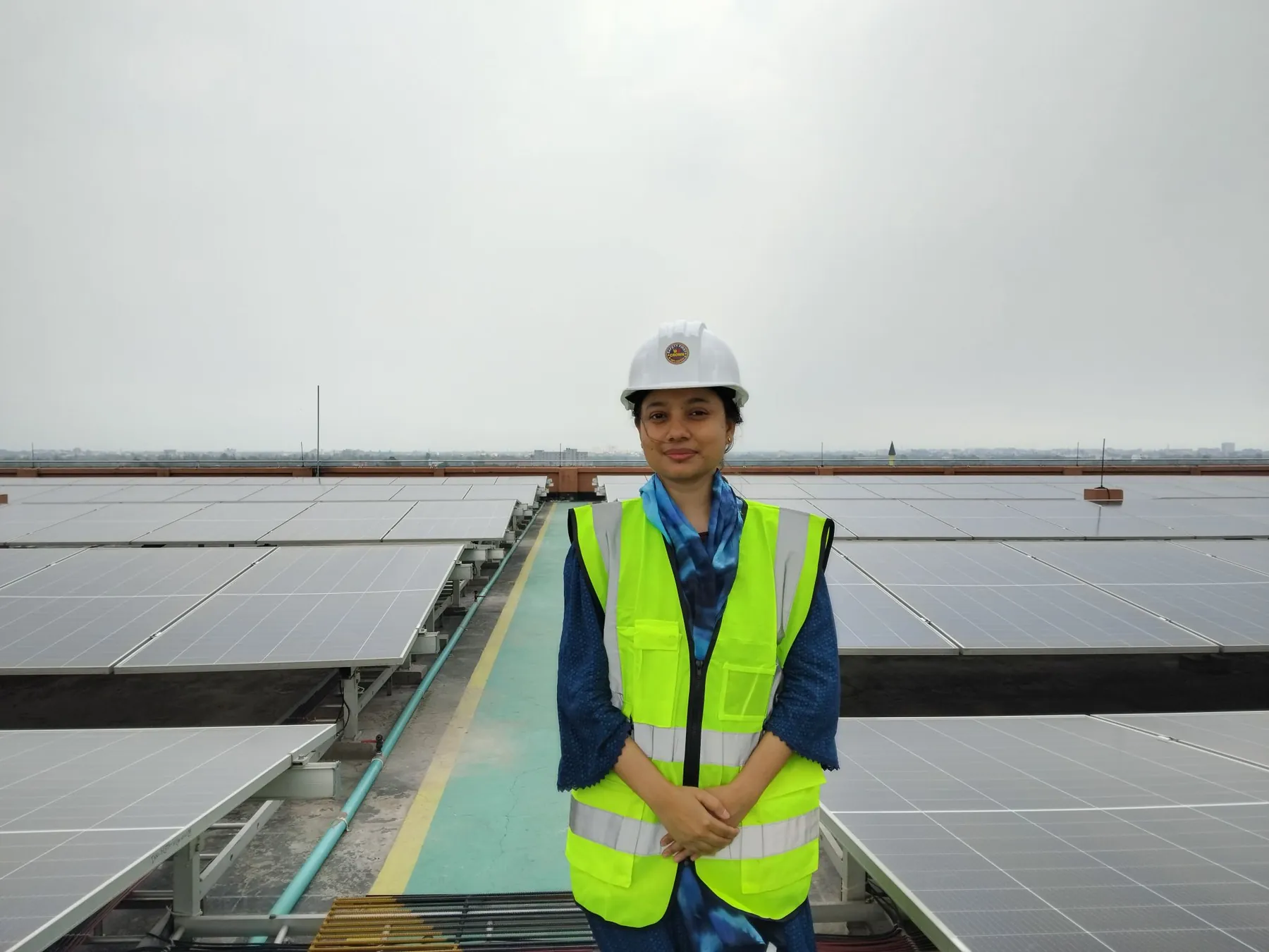 A Shoktikonna participant in a hard hat and safety vest on a rooftop solar plant
